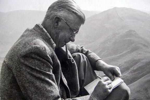 Alfred Wainwright sitting on a mountain writing in his notebook